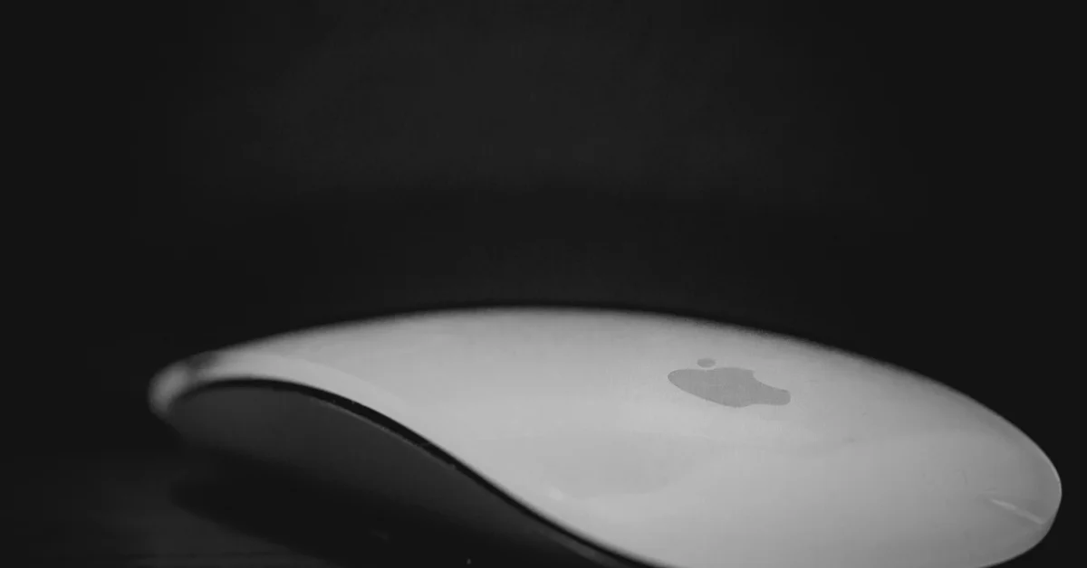 Close-up of a white Apple Magic Mouse with the Apple logo visible against a dark background.