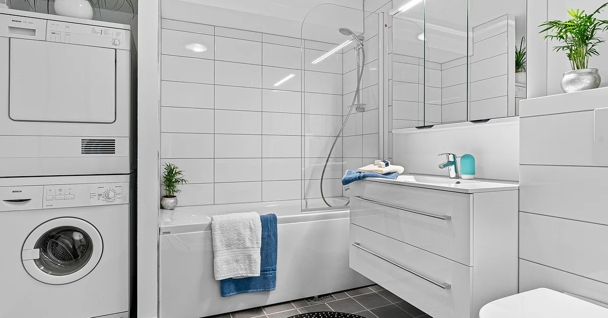 Modern bathroom with a stacked washer and dryer on the left, a glass-enclosed shower, and a white vanity, illustrating a clean, organized space as context for alternatives to using dryer sheets to repel mice.