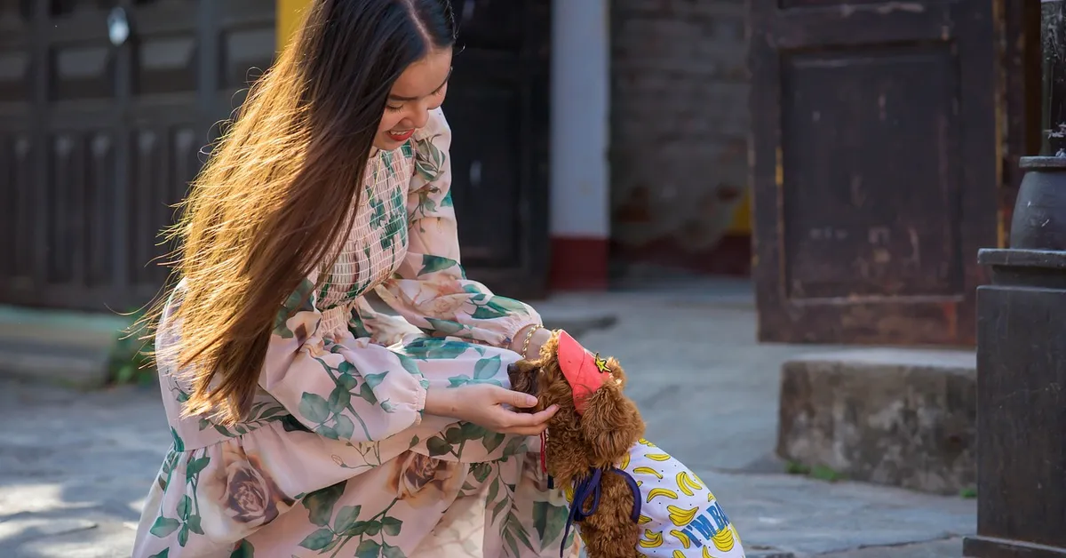 A woman in a floral dress gently cradles a small dog outdoors, illustrating calm and patient handling during bonding.