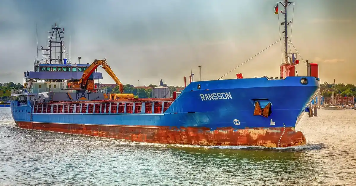 Blue cargo ship named Ransson sailing in a harbor with a rust-streaked hull and a crane on the deck.