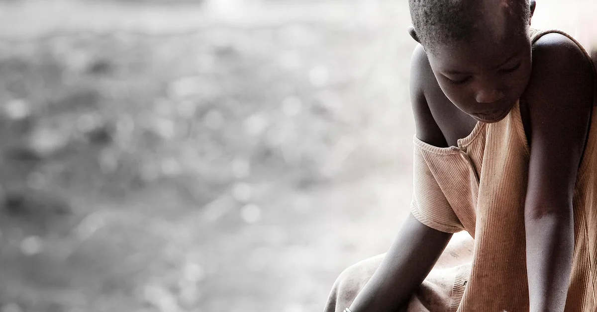 A young child sits with shoulders slumped and head bowed, looking down in a quiet, somber moment.