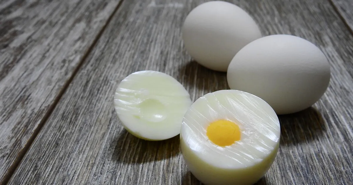 Several white eggs on a wooden surface, with one egg cut in half to reveal the yolk and surrounding white.