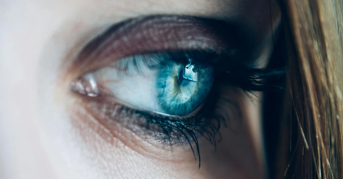 Macro image of a blue eye with long eyelashes, illustrating irritation and potential signs of conjunctivitis.