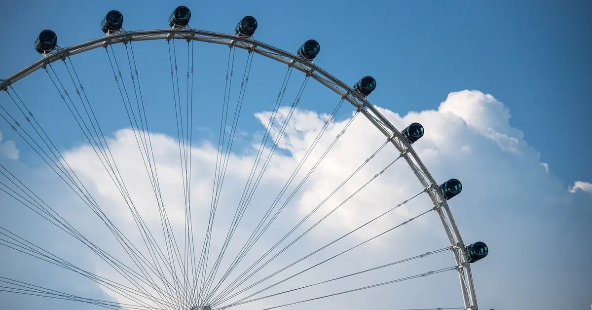 Ferris wheel with passenger capsules against a blue sky with clouds