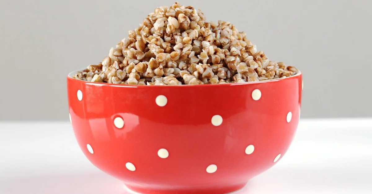 Red ceramic bowl with white polka dots overflowing with grain kernels on a light, clean surface