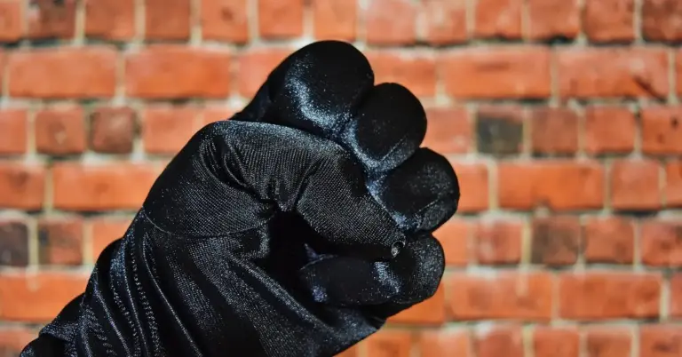 A gloved hand forming a fist in a threatening gesture against a brick wall.