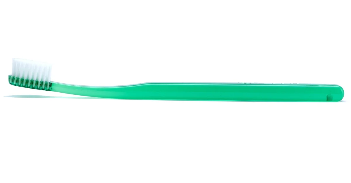 Green toothbrush laid horizontally on a white background
