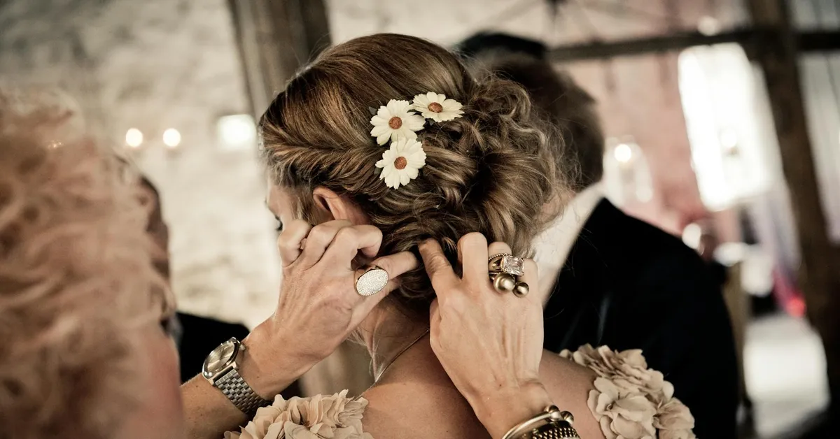 Close-up of a person’s hairstyle being adjusted, with braided hair and white daisy hair accessories, wearing rings and bracelets.
