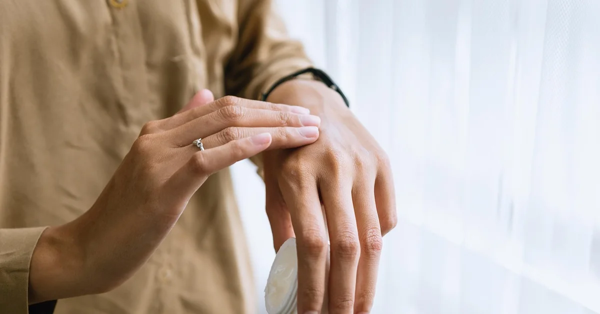 Person applying cream on hand, indicating personal grooming and health care.
