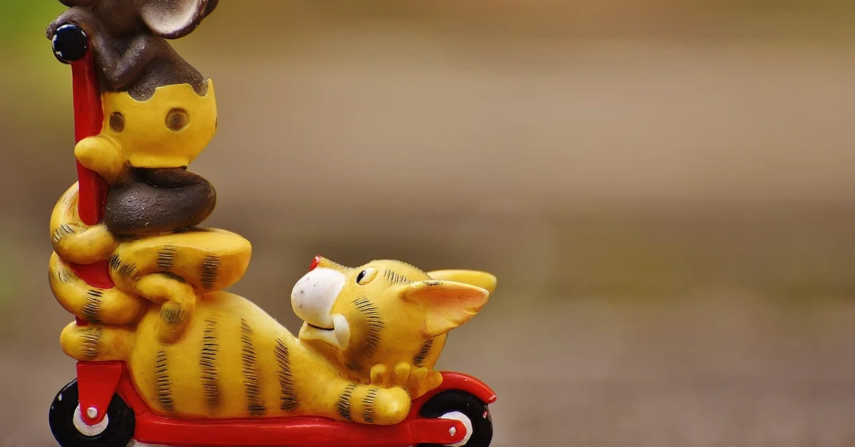 Cartoonish yellow mice on a red scooter, with one mouse seated on the front and another standing behind, against a blurred outdoor background.