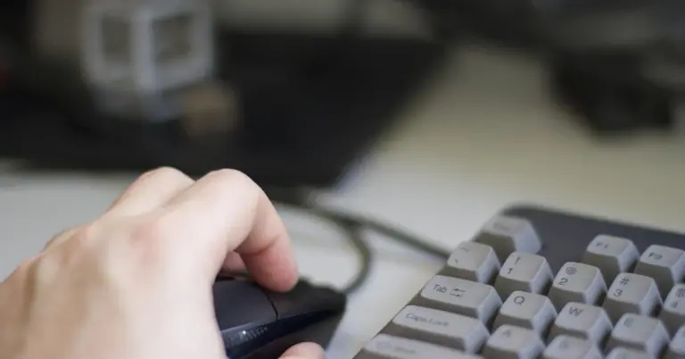 Close-up of a researcher’s hand on a computer mouse beside a keyboard in a laboratory setting