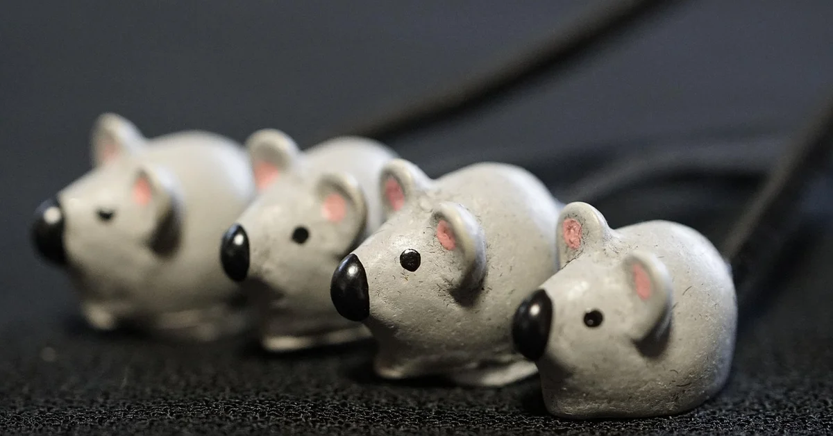 Four small gray toy mice with pink ears on a dark surface