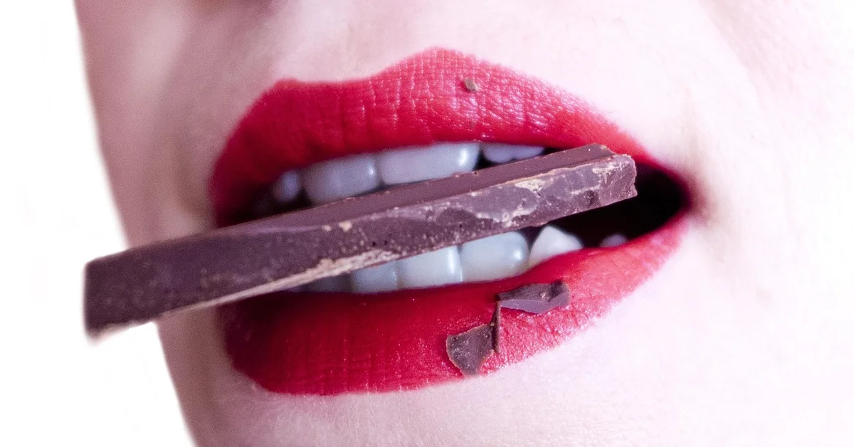 Close-up of red lips biting a chocolate bar held between teeth