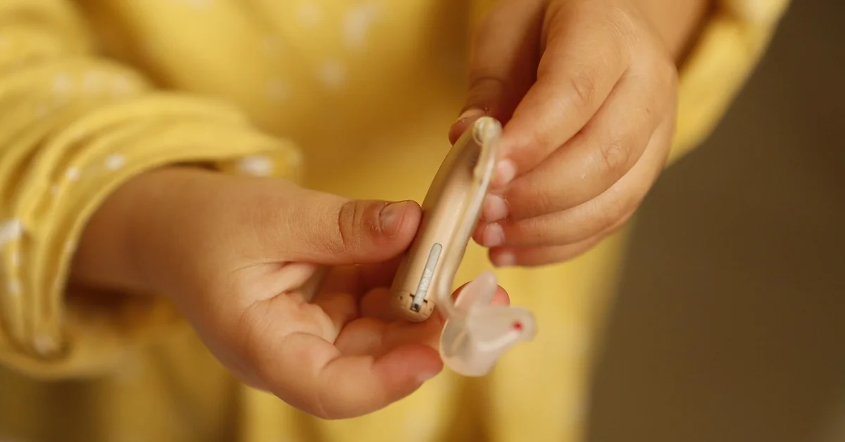 Close-up of hands holding a small medical device and an ear examination tool, suggesting monitoring a mouse's ear health