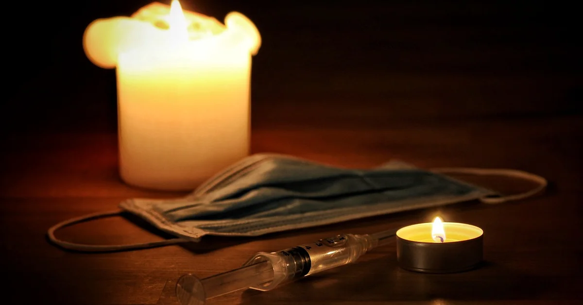 Close-up of a lit candle, a medical mask, and a syringe on a wooden surface, symbolizing end-of-life care for a pet mouse.