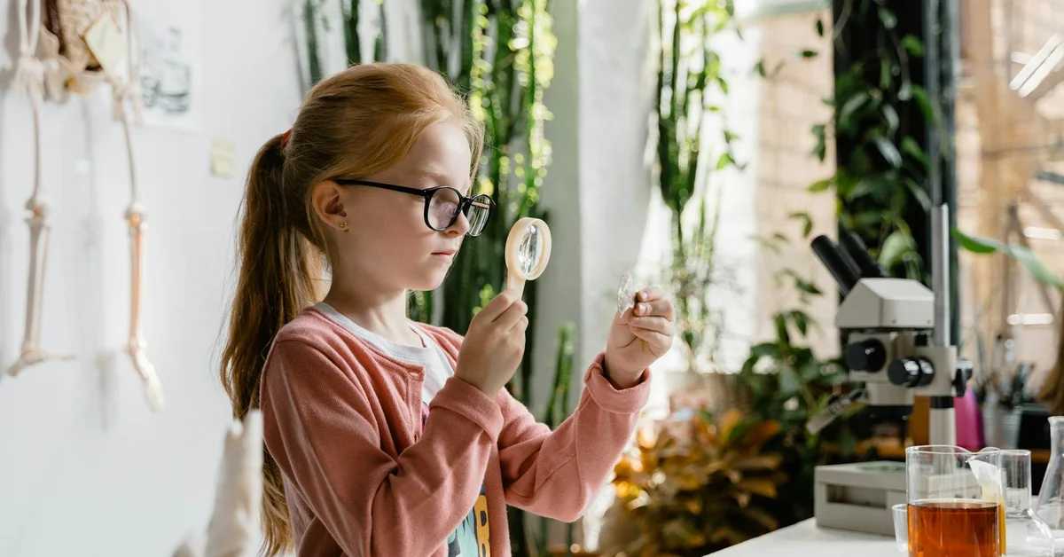 A young girl using a magnifying glass to examine a specimen in a laboratory setting.