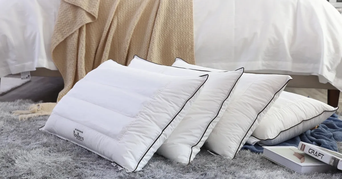 A set of white pillows stacked on a soft rug, with a blanket and bedding in the background.