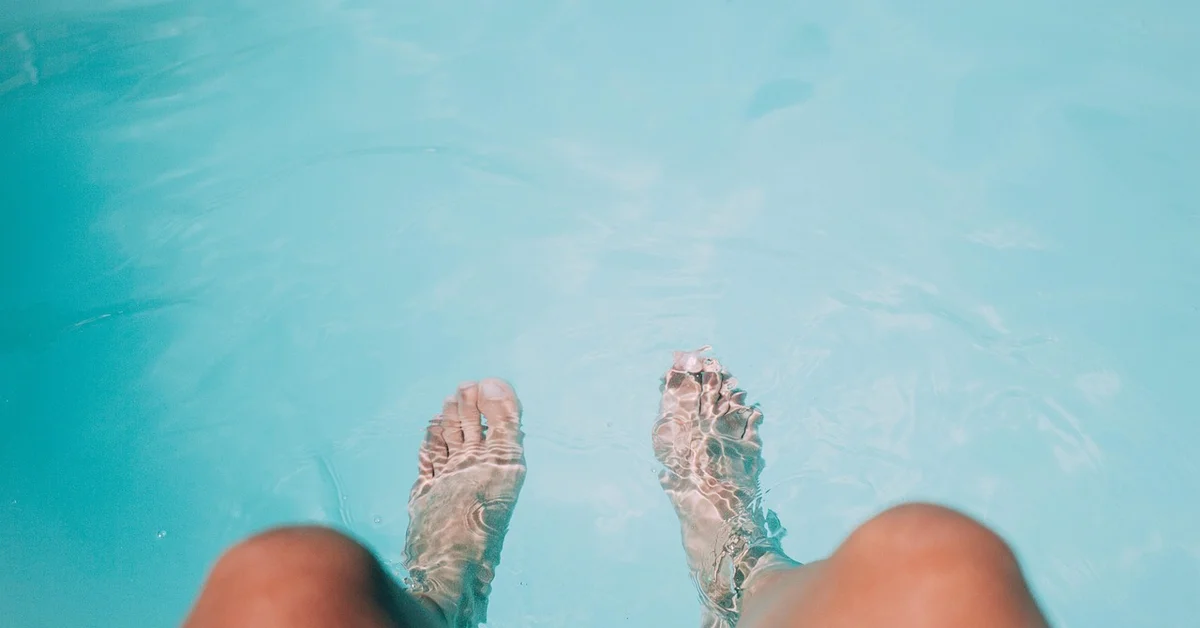 Bare feet submerged in a clear blue pool with light reflections on the water surface