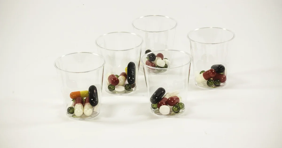 Clear plastic cups filled with assorted capsules and tablets on a white surface.
