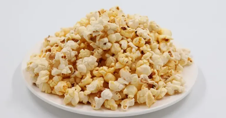 Pile of popped popcorn on a white plate against a pale background