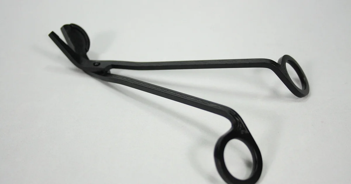 Close-up of a black ring-handled surgical instrument with two circular finger rings on a white surface, used in mouse surgery preparation.