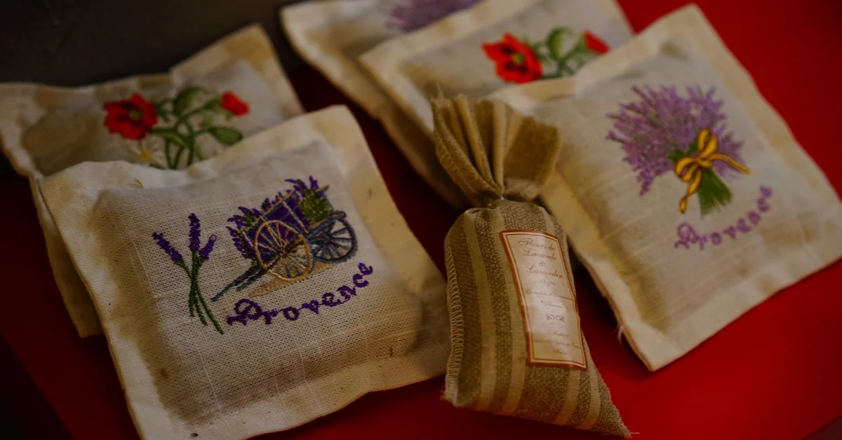 Several decorative fabric sachets with lavender, plants, and floral embroidery, plus a striped burlap bag, arranged on a red surface.