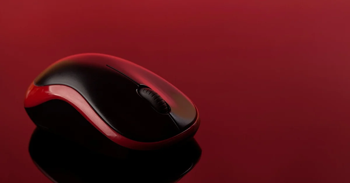 Glossy red-and-black computer mouse on a red reflective surface with a soft red background.