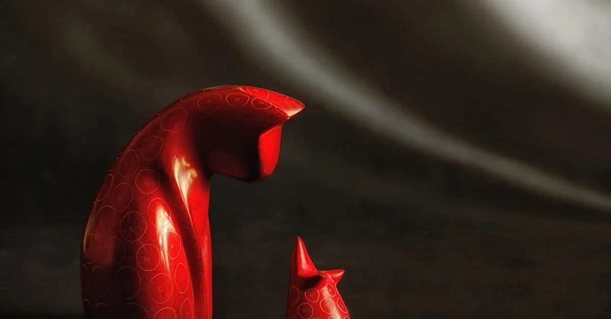 Abstract red sculpture resembling a large and a smaller mouse figure with circular patterns, set against a dark background.
