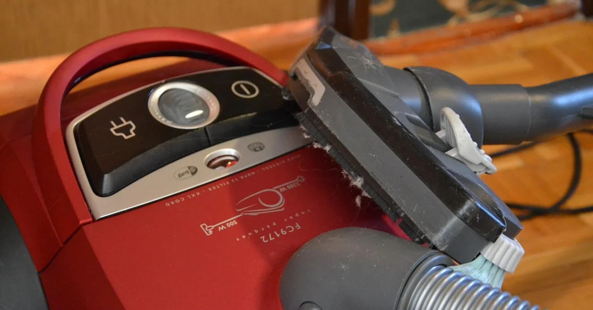 Close-up of a red vacuum cleaner with a cracked nozzle sitting on a wooden floor