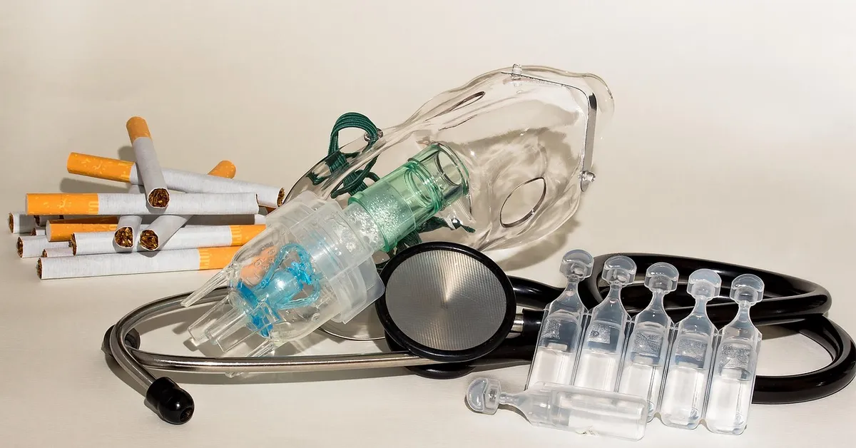 Still life of medical equipment for respiratory care: a stethoscope, a bag-valve-mask device, and clear vials, with cigarettes stacked in the background.