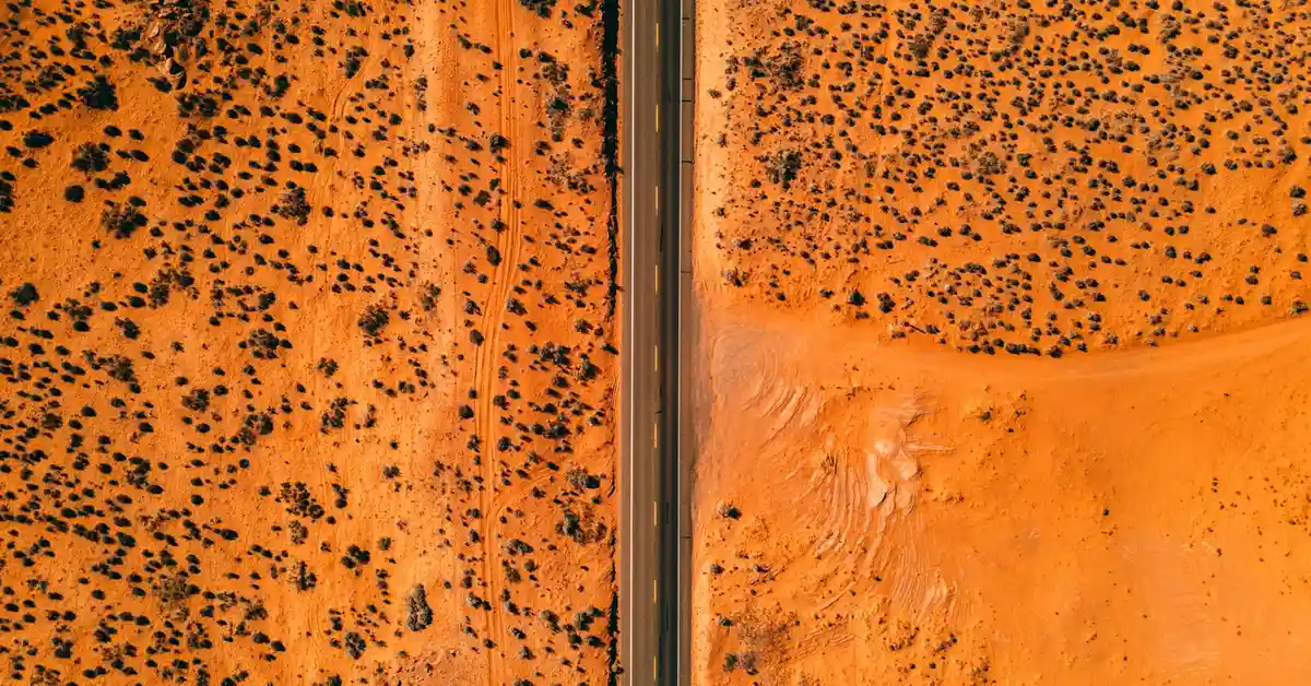 Aerial view of a desert landscape with a road dividing sandy terrain and sparse vegetation