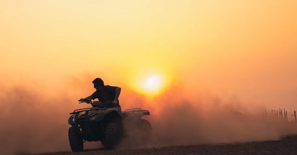 A person riding an ATV in a dusty environment during sunset