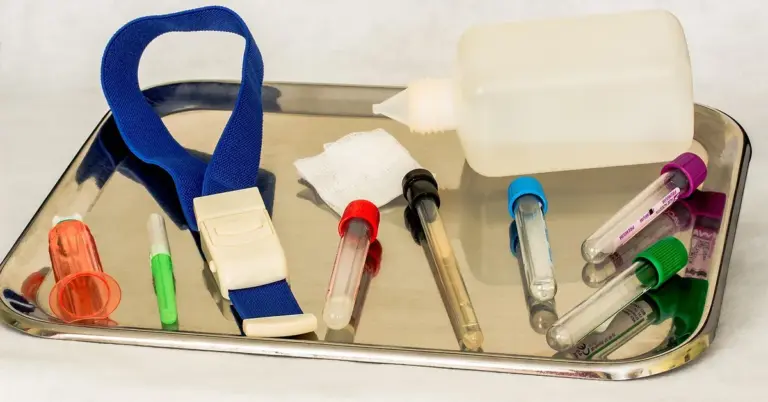 Veterinary blood collection tray with vials, syringes, gauze, and a bottle on a reflective metal tray.