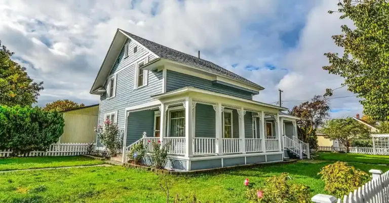 Blue two-story house with a white wraparound porch and a manicured lawn, representing a safe home environment for puppy socialization.