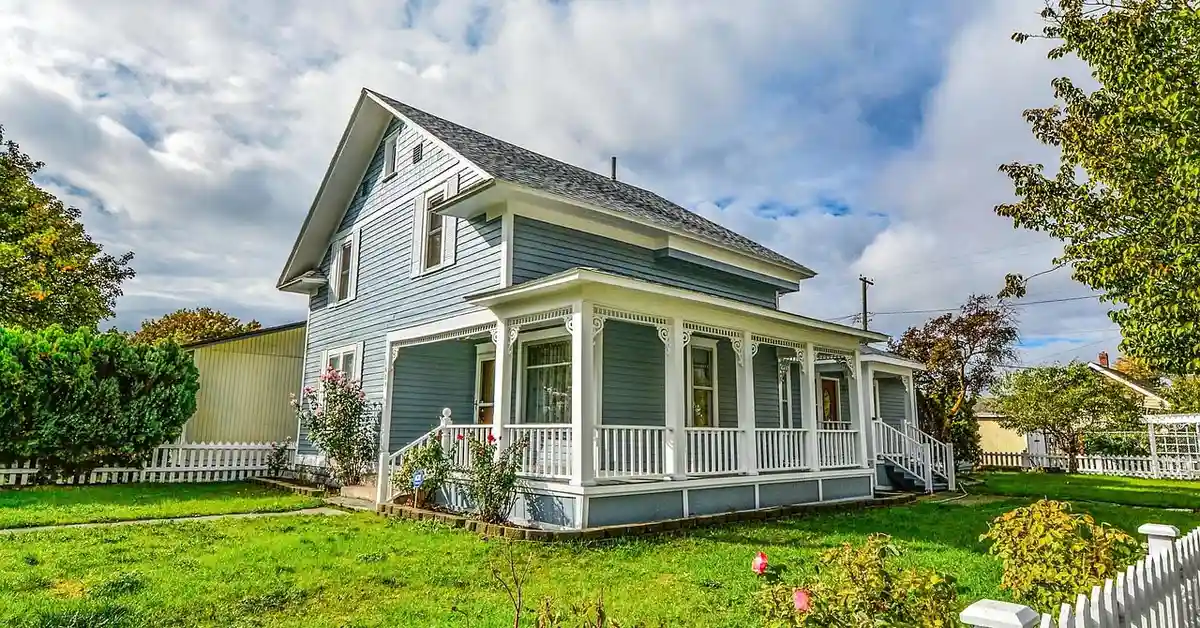 Blue two-story house with a white wraparound porch and a manicured lawn, representing a safe home environment for puppy socialization.