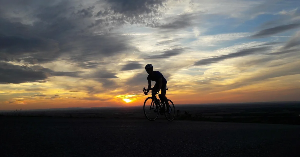 Silhouette of a cyclist riding a road bike against a sunset.