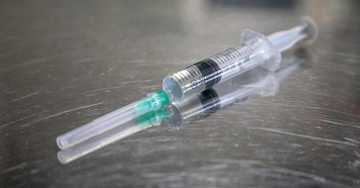 Close-up of a clear syringe with a green plunger on a stainless steel surface, prepared for syringe feeding.