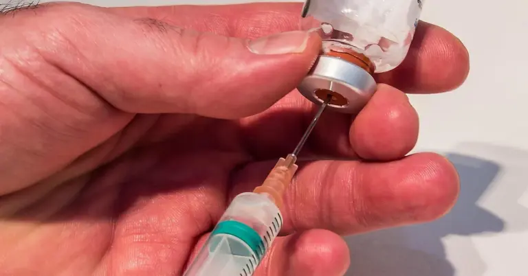 Close-up of a hand drawing liquid from a small vial into a syringe, illustrating syringe feeding and hydration in supportive care.