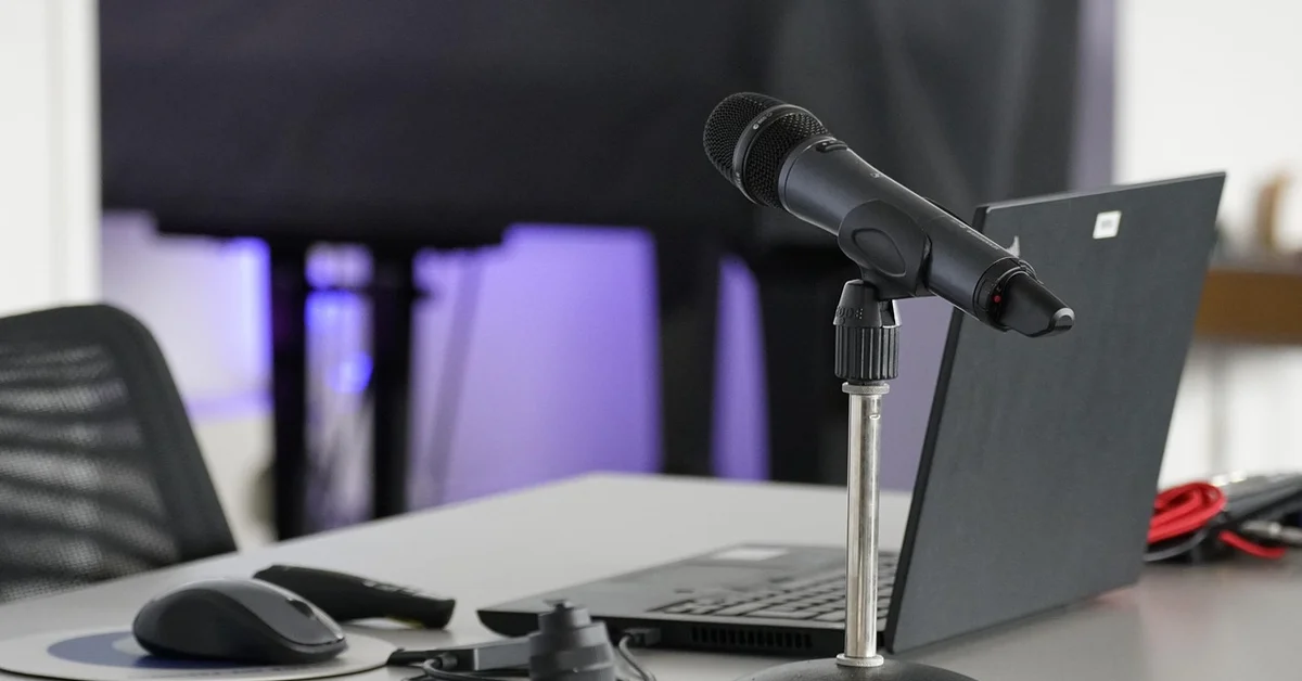 Close-up of a microphone on a stand in front of a laptop on a conference desk, ready for a podcast or interview.