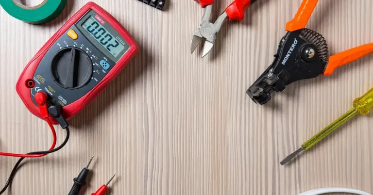 Assorted electrical tools on a wooden workbench, including a red digital multimeter, pliers, and wire cutters.