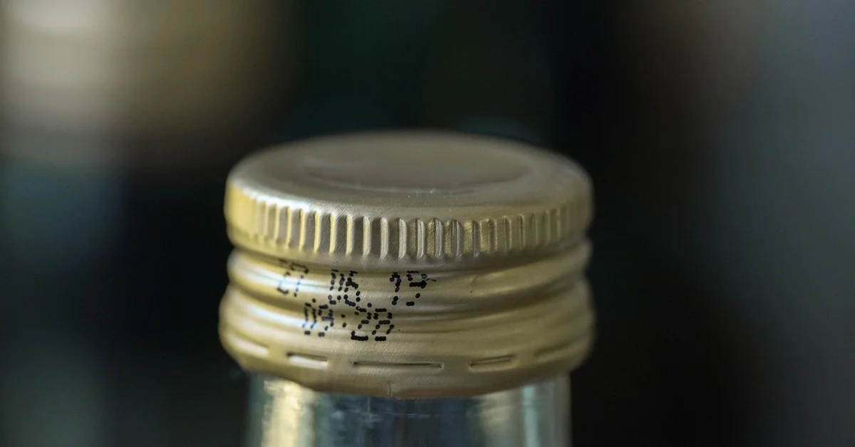 Close-up of a metal bottle cap on a glass water bottle, with a blurred background.