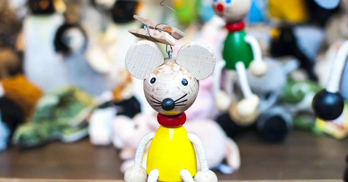 Wooden mouse-shaped enrichment toy featuring a yellow body, red neck, and white rope limbs, designed to rotate and engage a mouse.